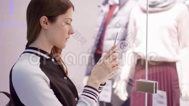 一个年轻的女人在橱窗店附近和男人。 通过智能手机阅读二维码，在线查看价格